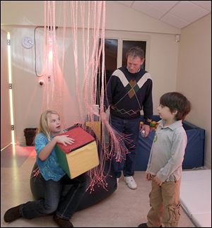 Sophia Rogers, 9, her brother Jack, 6, and their grandfather, Don Rogers of Mentor, Ohio, check out the Special Kids Therapy Playroom. The box Sophia holds controls the color of the light in the room, including the color of the fiber-optic cables hanging around her; the room has a reddish cast because the box’s red side is on top.