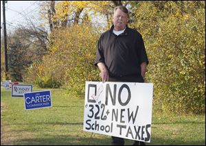 Phil Caron stands near his front yard sign in opposition to the Perrysburg school levy.