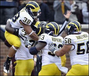 Michigan's A.J. Williams, second from left second, hoists running back Thomas Rawls (38) after Rawls scored a touchdown against Minnesota during the second quarter of an NCAA college football game, Saturday, in Minneapolis. Michigan's Stephen Hopkins (33) and Joey Burzynski (56) join the celebration.