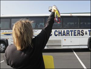 Parent Julie Olmstead waves and rings a bell as the students depart. She made a cowbell for each player, and one for the coaches and players' siblings. She also is hosting a [free] tailgate for Yellow Jacket fans with 120 hot dogs, 120 hamburgers and 60 brats at the game. She is the parent of Rachael Olmstead, a junior midfielder.