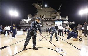 Military personnel and volunteers wipe off condensation in an attempt to dry the damp court before the start of the game between Ohio Sate and Marquette aboard the USS Yorktown. Officials called off the game because of the damp court.