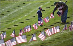 Joseph Manning, right, of Raynham, Mass., and his son Joey, 6, a Cub Scout, place U.S. flags at the graves of deceased veterans today at the National Cemetery in Bourne, Mass.