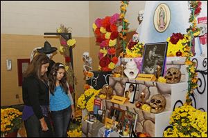 Tracey Martinez, of Monclova, left, and her daughter Serena Yerg, 13, look at the alter with photographs and remembrances of three members of the Latin American community who have died in the past year during Saturday evening's 16th annual Dia de los Muertos (Day of the Dead) celebration at the Aurora Gonzalez Believe Center in Toledo.