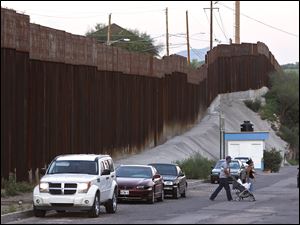 In this Aug. 9, 2012, photo, vehicles are parked along the border fence as pedestrians cross the street in Nogales, Mexico. The location is near the site where a U.S. Border Patrol agent being pelted with rocks opened fire toward Mexico, killing a 16-year-old boy. The shooting has prompted renewed outcry over the Border Patrol’s use-of-force policies and angered human rights activists and Mexican officials who believe the incident has become part of a disturbing trend along the border _ gunning down rock-throwers rather than using non-lethal weapons. (AP Photo/Ross D. Franklin)