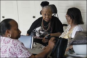 Laura Gipson, center, shares a moment with Carolyn Mason, right, in the community room of Alpha Towers. Ms. Gipson said she recently waited six hours for staff to operate an elevator.