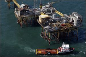 In this aerial photograph, a supply vessel moves near an oil rig damaged by an explosion and fire, Friday, Nov. 16, 2012, in the Gulf of Mexico about 25 miles southeast of Grand Isle, La. Four people were transported to a hospital with critical burns and two were missing. (AP Photo/Gerald Herbert)