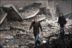 Palestinians walk through the debris after an Israeli air strike on building in Gaza City, Sunday. The Israeli military widened its range of targets in the Gaza Strip on Sunday to include the media operations of the Palestinian territory's Hamas rulers.