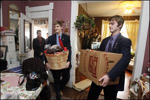Laurie Yeager, in doorway, her son Peter Yeager, and Marc Elfering carry food into the East Toledo home of Angie Graves and her family. St. Francis students delivered about 50 baskets on Tuesday to area families. The baskets are expected to feed nearly 300 people over the holiday.