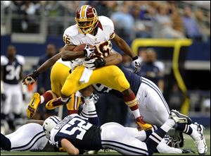 Washington Redskins running back Alfred Morris leaps over Dallas Cowboys' Dan Connor (52) as he tries to escape a tackle by Jason Hatcher, rear, in the first half today in Arlington, Texas.