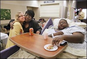 Nurse Tamara Smith is embraced by Deborah Adeyemi, mother of Anthony Taylor, right, as Mr. Taylor samples dessert from the Thanksgiving Day meal. A recent surgery prevented Mr. Taylor from going home for the holiday, so it came to him.
