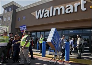 Shopper Jose Alvarez carries out a newly-purchased television past protestors Friday outside a Walmart store in Paramount, Calif.