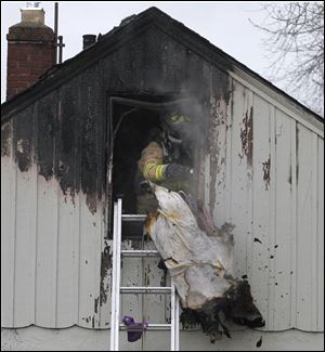 A Sylvania firefighter throws burnt debris out from an attic at Balfour Rd. in Sylvania, Ohio.