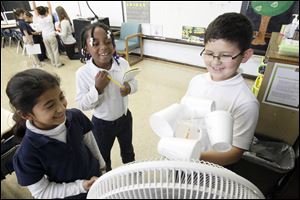 Second graders Selena Garcia, left, and Heaven Williams, center, and Ruben Angel, right, use an anemometer and a fan to collect data so that they can predict weather for a lesson.