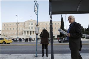 A man reads a newspaper as he walks past a bus stop opposite the Parliament in central Athens today.