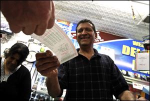 As he hands over a customer's lottery ticket, Keith Ganatra, right, and his wife Anita Ganatra, left, owners of the Del Monte Market, help the long line of customers inside their store waiting to buy Powerball lottery tickets Wednesday, in Phoenix.