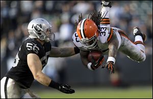 Cleveland Browns running back Trent Richardson, right, leaps in front of Oakland Raiders linebacker Miles Burris during the third quarter Sunday in Oakland, Calif. The Browns won 20-17, snapping a 12-game road losing streak.