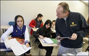 Instructor Michael Klug, right, checks the work of LiYan Ji,  left, during an American Language Institute English class at the University of Toledo, as Yuan Fang, back left, Ruihan Hu, and Min Dong work.