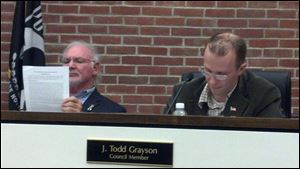 Perrysburg City Council president Joseph Lawless, left, looks over the minutes of the Health, Sanitation, and Public Utilities Committee as its chairman J. Todd Grayson, right, reads them into the record at the city council meeting Tuesday.