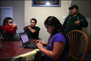 Leslie Mendoza uses a laptop as her father, Felipe, right, his nephew Aaron Carillo and Carillo's son, Jayden, talk in the home htey rent in Aurora, Illinois. Some are turning foreclosed homes into investments by buying and turning them into rental properties.