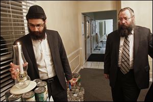 ﻿Rabbi Shmouel Matusof, left, lights a single candle atop the base of a menorah being crafted from cans of kosher food as his father-in-law, Rabbi Yossi Shemtov, looks on. The canned goods, donated by members of the Jewish community, will be donated at the end of the eight-day Festival of Lights.
