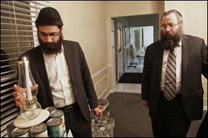 Rabbi Shmouel Matusof, left, lights a single candle atop the base of a menorah being crafted from cans of kosher food as his father-in-law, Rabbi Yossi Shemtov, looks on. The canned goods, donated by members of the Jewish community, will be donated at the end of the eight-day Festival of Lights.
