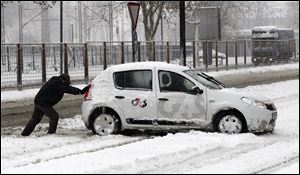 A man pushes a car on a snow covered street in Belgrade, Serbia, Sunday.