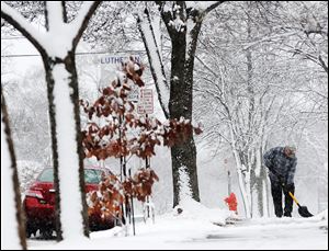 Jean Bohlinger shovels snow from the sidewalk in front of his daughter's house, Sunday, in Winona, Minn. 