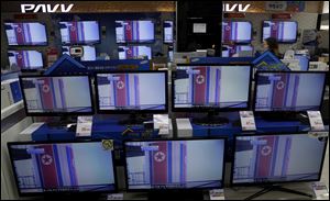 A clerk passes by TV screens, airing file footage and reporting about North Korea's rocket launch, at an electronic shop in Seoul, South Korea.
