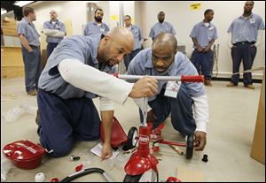 Inmates Rubin Johnson III, left, and Thomas Claybourne assemble a donated tricycle. It is one of those to be given to children who are served by Lucas County Children Services.