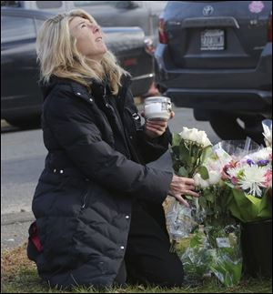 A woman pauses to place flowers and a candle at a makeshift memorial outside the Sandy Hook school. Memorial services have begun for the 20 children and six adults killed there.