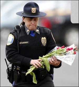 Newtown Police Officer Maryhelen McCarthy places flowers at a makeshift memorial outside St. Rose of Lima Roman Catholic Church, Sunday, Dec. 16, 2012, in Newtown, Conn. On Friday, a gunman allegedly killed his mother at their home and then opened fire inside the Sandy Hook Elementary School, killing 26 people, including 20 children. (AP Photo/Julio Cortez)