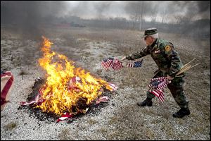 Larry Barnett of the Marine Corps League Lou Diamond Detachment #272 throws a handful of U.S. flags into the fire, the correct way to dispose of flags.