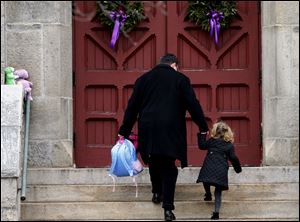 A man helps a young girl up the stairs while carrying her backpack as they arrive for services at Trinity Church in Newtown, Conn., on Sunday. 