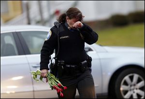 Newtown Police Officer Maryhelen McCarthy carries flowers near a memorial for shooting victims Sunday, Dec. 16, 2012 in Newtown, Conn.  A gunman walked into Sandy Hook Elementary School in Newtown, Friday and opened fire, killing 26 people, including 20 children. The flowers and other items were taken to nearby Saint Rose of Lima Roman Catholic Church.