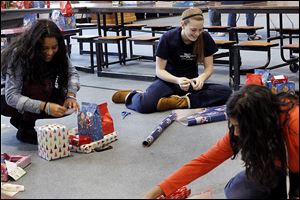 Grisoranyel Barrios, 17, left, jokes with Carolyn Manley, 17, center, as the pair join their classmates in wrapping presents for children at Providence Lutheran Church in  Springfield Twp.