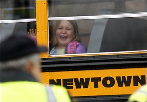 A young girl waves as her school bus pulls into Hawley School, today in Newtown, Conn.  Classes resume for Newtown schools except those at Sandy Hook.