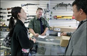 Todd Bruning, center, owner of Todd's Guns in Lambertville, speaks with Melissa Green and her father-in-law, Mark Busby, as he sells Ms. Green, who is soon to receive a teaching degree, a gun. She says educators should be able to carry a gun to protect their students.