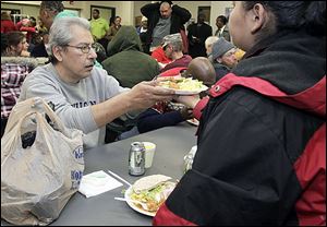 Another diner passes a meal to Gaspar Rodriguez, left, of Toledo at St. Paul's Community Center during its Christmas dinner for residents and guests Monday.