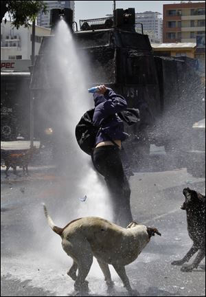 Dogs bark as a hooded youth gets into position to throw a bottle filled with paint as he is sprayed by a police water cannon in Santiago, Chile, in October.