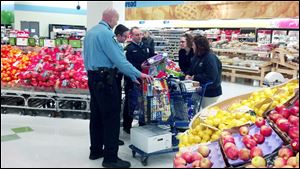 Police officers load a cart at Meijer on East Alexis Road to replace gifts for Nicole Kosci­uczyk’s four children that were stolen in a burglary Monday.