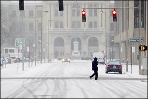 A lone pedestrian crosses North Ontario Street near the Lucas County Courthouse as snow starts to blanket downtown Toledo.