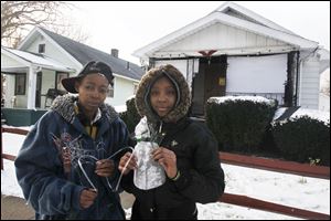 Courtney Brewer, left, and her daughter Oneisha Williams, 15, hold the mask used by firefighters to save a dog outside of its Buckeye Street.  The dog's home is in the background at right. Brewer and Williams live in the house at left.