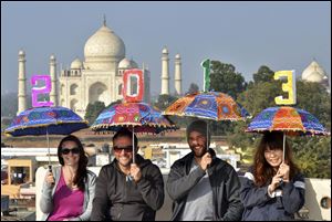 Tourists pose as they carry umbrellas with numbers to welcome the New Year 2013 on the terrace of a hotel in the backdrop of Taj Mahal in Agra, India.