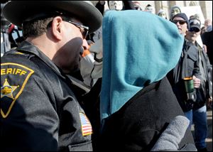 A masked participant hugs Jefferson County Sheriff Fred Abdalla during the rally at Steubenville City Hall. The sheriff, who wore a teal ribbon, a sign of support for rape victims, came under fire from many in the crowd.