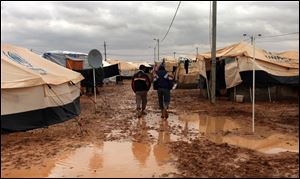 Two Syrian refugees walk among tents, surrounded by water and mud, at Zaatari Syrian refugee camp, near the Syrian border in Mafraq, Jordan, Tuesday, Jan. 8, 2013. Syrian refugees in a Jordanian camp attacked aid workers with sticks and stones on Tuesday, frustrated after cold, howling winds swept away their tents and torrential rains flooded muddy streets overnight. Police said seven aid workers were injured. (AP Photo/Mohammad Hannon)
