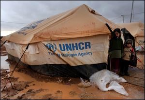 Syrian refugee children stand near their tent, surrounded by water and mud, at Zaatari Syrian refugee camp, near the Syrian border in Mafraq, Jordan, Tuesday, Jan. 8, 2013. Syrian refugees in a Jordanian camp attacked aid workers with sticks and stones on Tuesday, frustrated after cold, howling winds swept away their tents and torrential rains flooded muddy streets overnight. Police said seven aid workers were injured. (AP Photo/Mohammad Hannon)