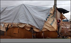 A Syrian refugee woman looks out of her tent surrounded with water and mud, at Zaatari Syrian refugee camp, near the Syrian border in Mafraq, Jordan, Tuesday, Jan. 8, 2013. Syrian refugees in a Jordanian camp attacked aid workers with sticks and stones on Tuesday, frustrated after cold, howling winds swept away their tents and torrential rains flooded muddy streets overnight. Police said seven aid workers were injured. (AP Photo/Mohammad Hannon)