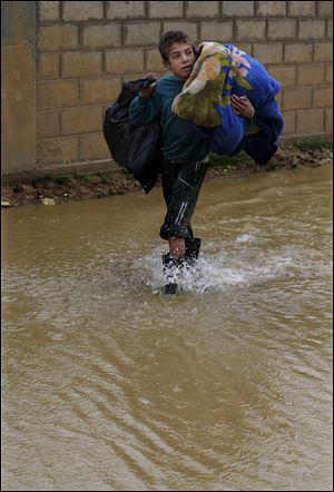 A Syrian refugee boy carries his belongings as he makes his way in flooded water at a temporary refugee camp, in the eastern Lebanese Town of Al-Faour near the border with Syria, Lebanon, Tuesday, Jan. 8, 2013. Two Syrian refugee encampments in Lebanon’s eastern Bekaa valley  were completely immersed in water Tuesday after the Litani river flooded and the water came pouring into their tents. The flood forced dozens of Syrian refugees to leave in search for alternative shelter along with their water-soaked and muddied belongings. (AP Photo/Hussein Malla)