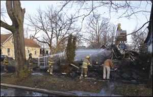 Toledo firefighters pour water on a house as Toledo city workers demolish it on Fernwood Avenue.