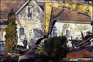 James Harris, left, and his cousin, Addie Mae Williams stand near the home of his father, James Harris, as they watch a city crew demolish a house that caught fire at 1058 Fernwood Ave.